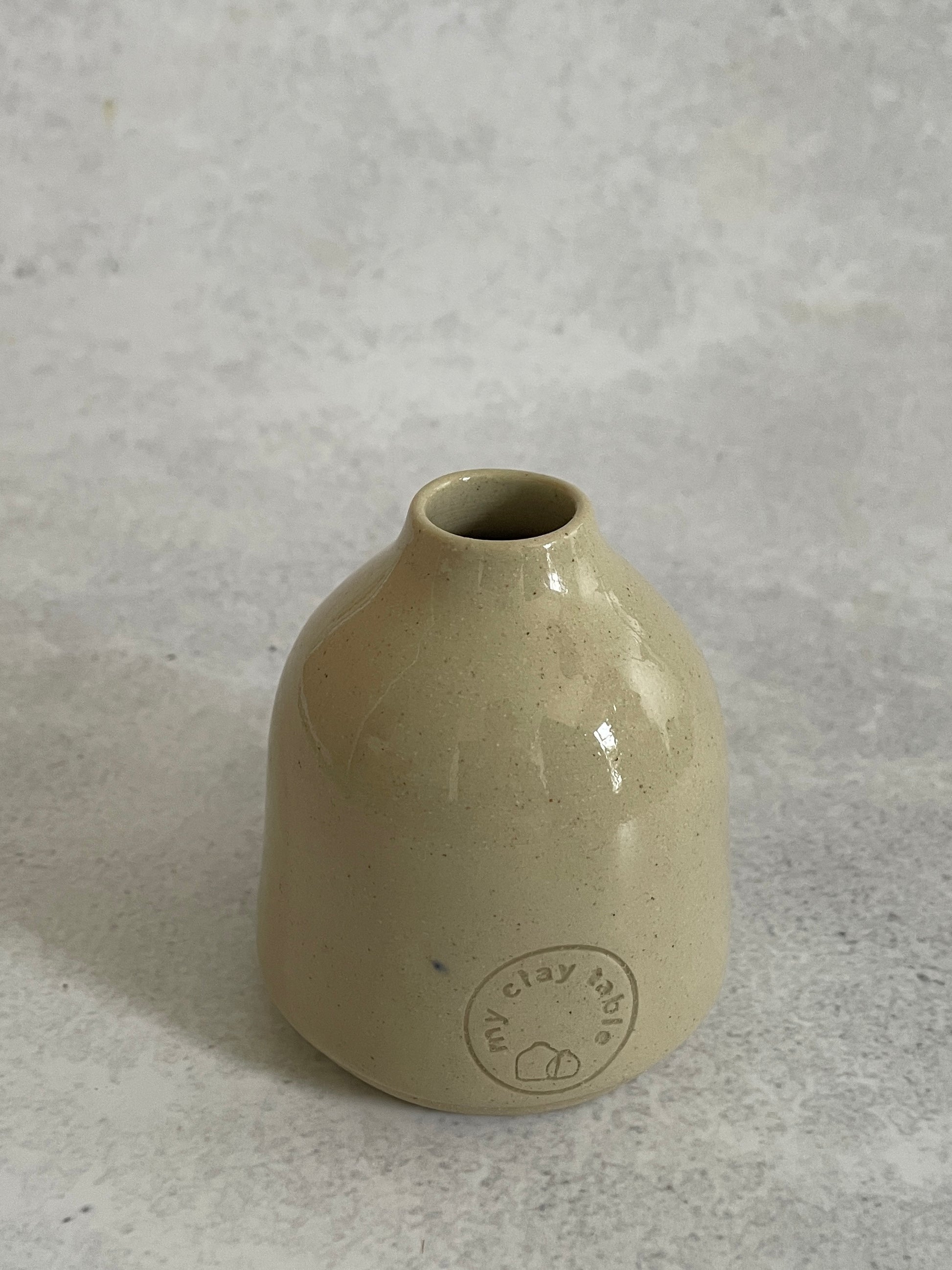 Beige ceramic vase with a circular logo on a gray background